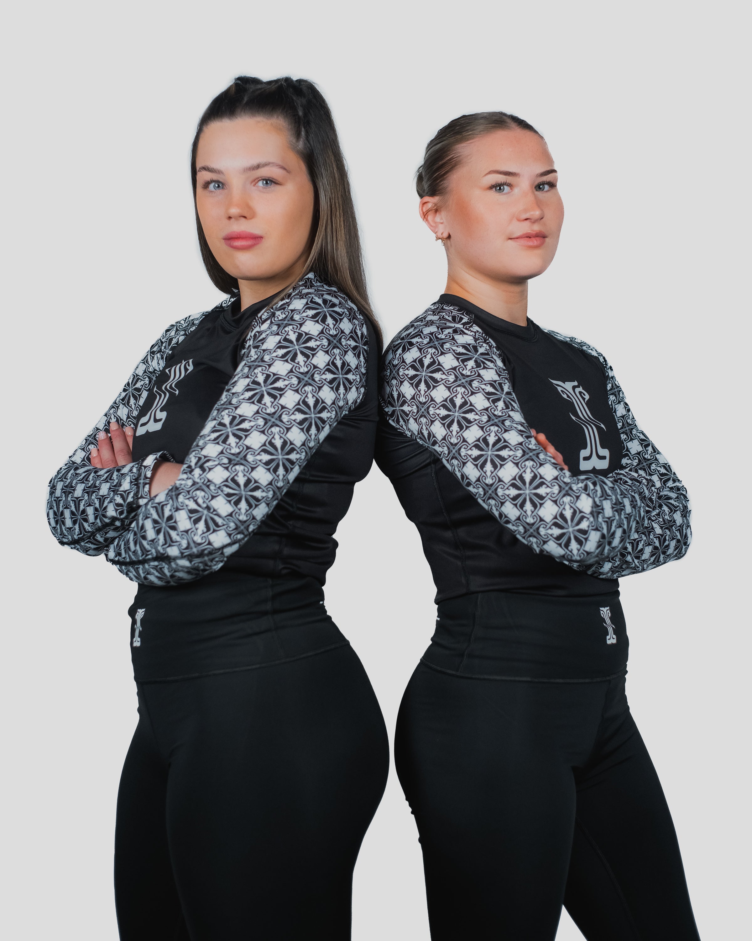 Two female athletes in the Gorgo Long Sleeve Rash Guard with arms crossed, emphasising the sleek fit and striking sleeve pattern.
