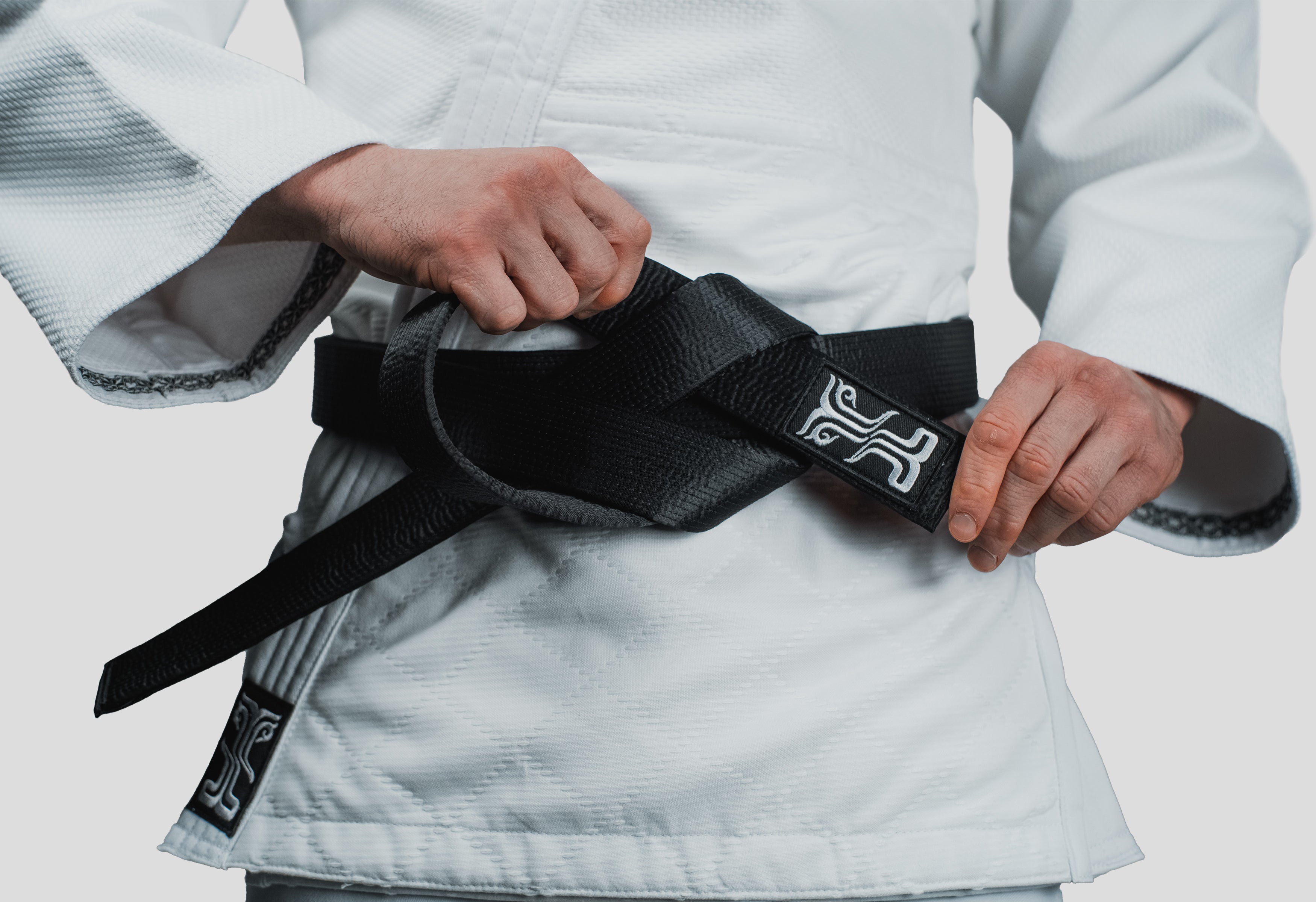 Close-up of the Phobos Black Judo Belt being tied, featuring the embroidered Kosmos logo and high-quality weave