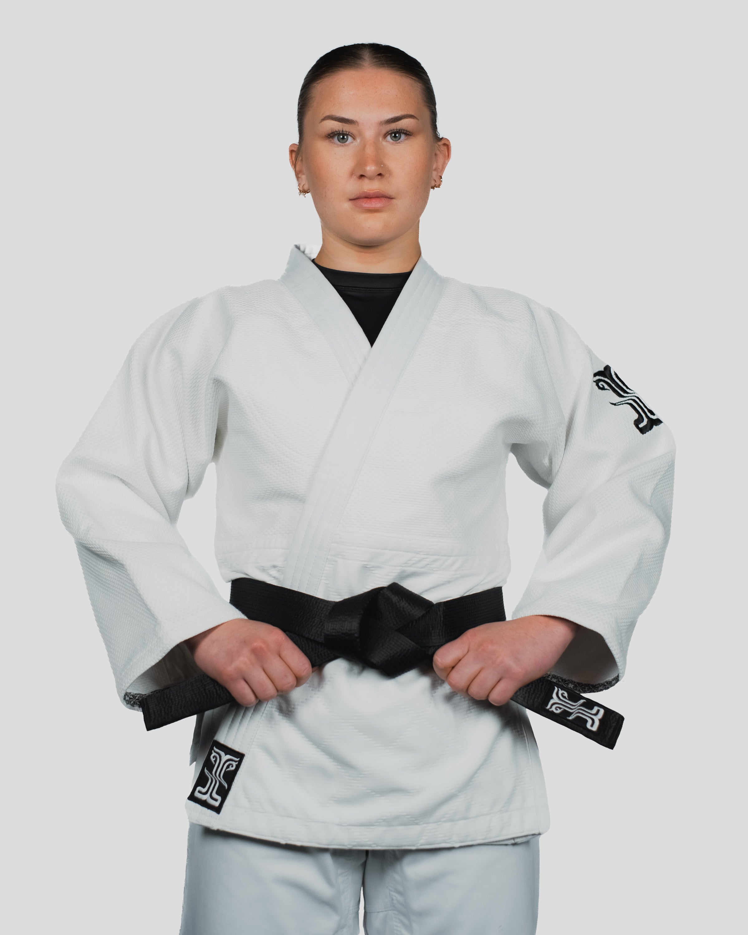 Female martial artist wearing the Stoa Gi Women's Judo uniform with a black belt, standing in a confident front stance