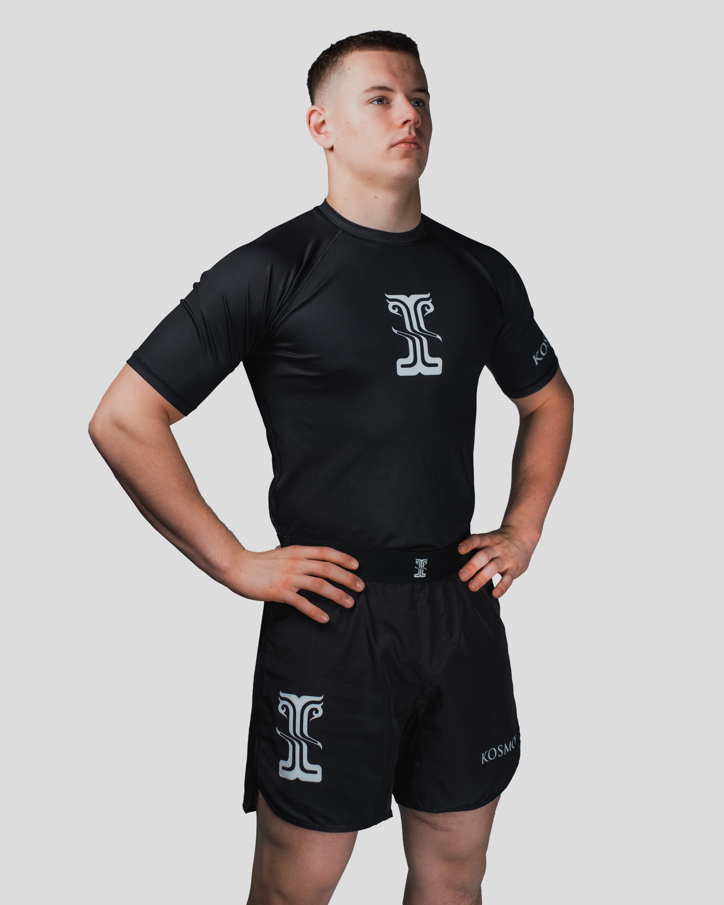Side profile of the Column Shorts, showing the sleek black fabric and Kosmos emblem placement