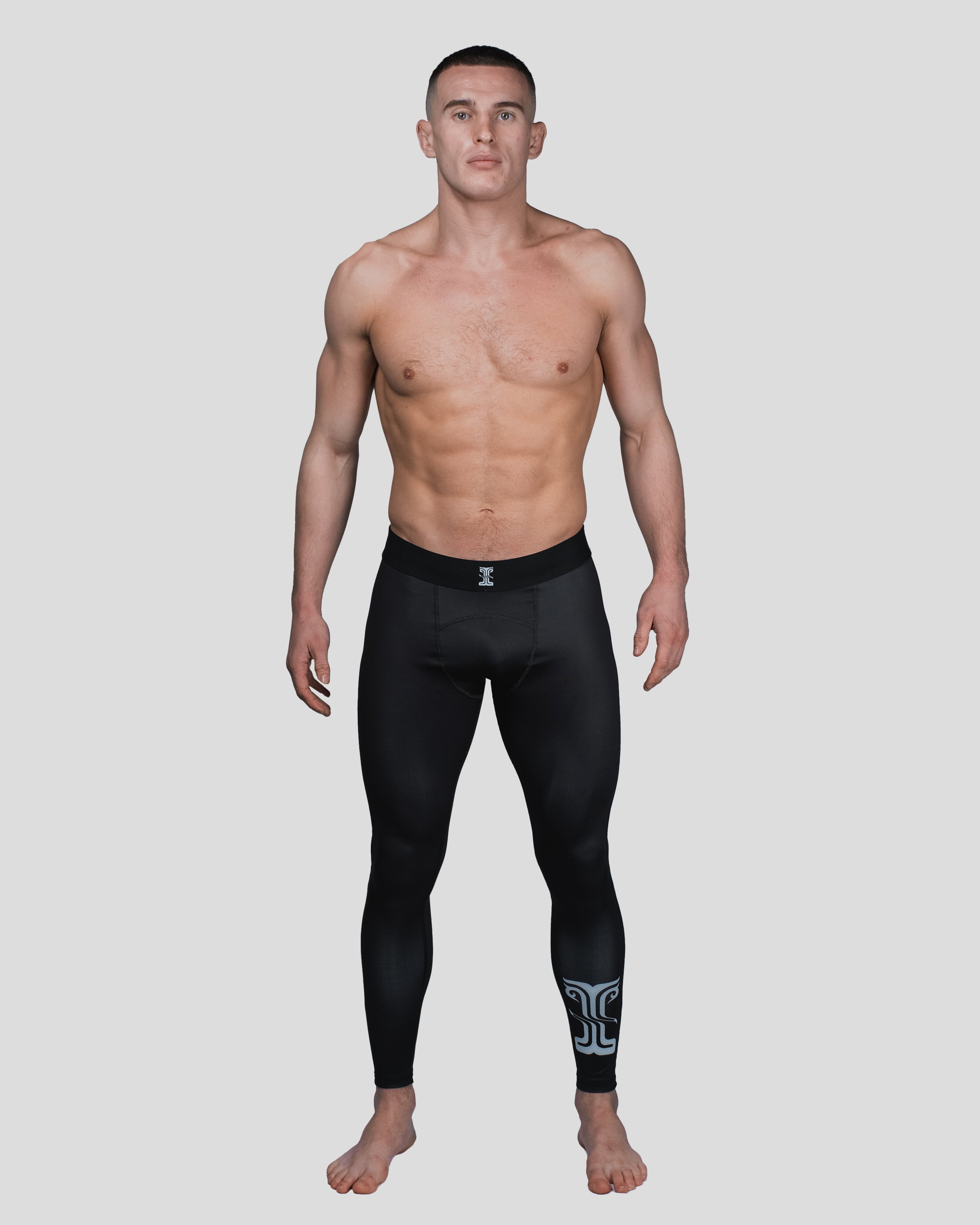 Full-body shot of a male model wearing the Column Spats, showcasing the sleek black compression fit with a white logo on the lower leg