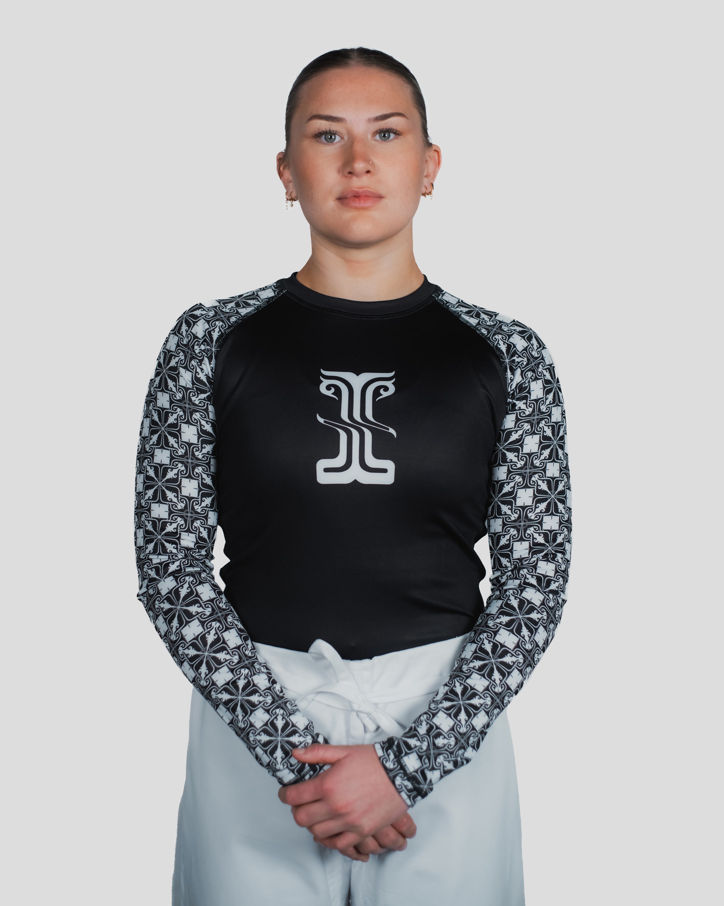 Female model wearing the Gorgo Long Sleeve Rash Guard, showcasing the bold front logo and intricate sleeve pattern