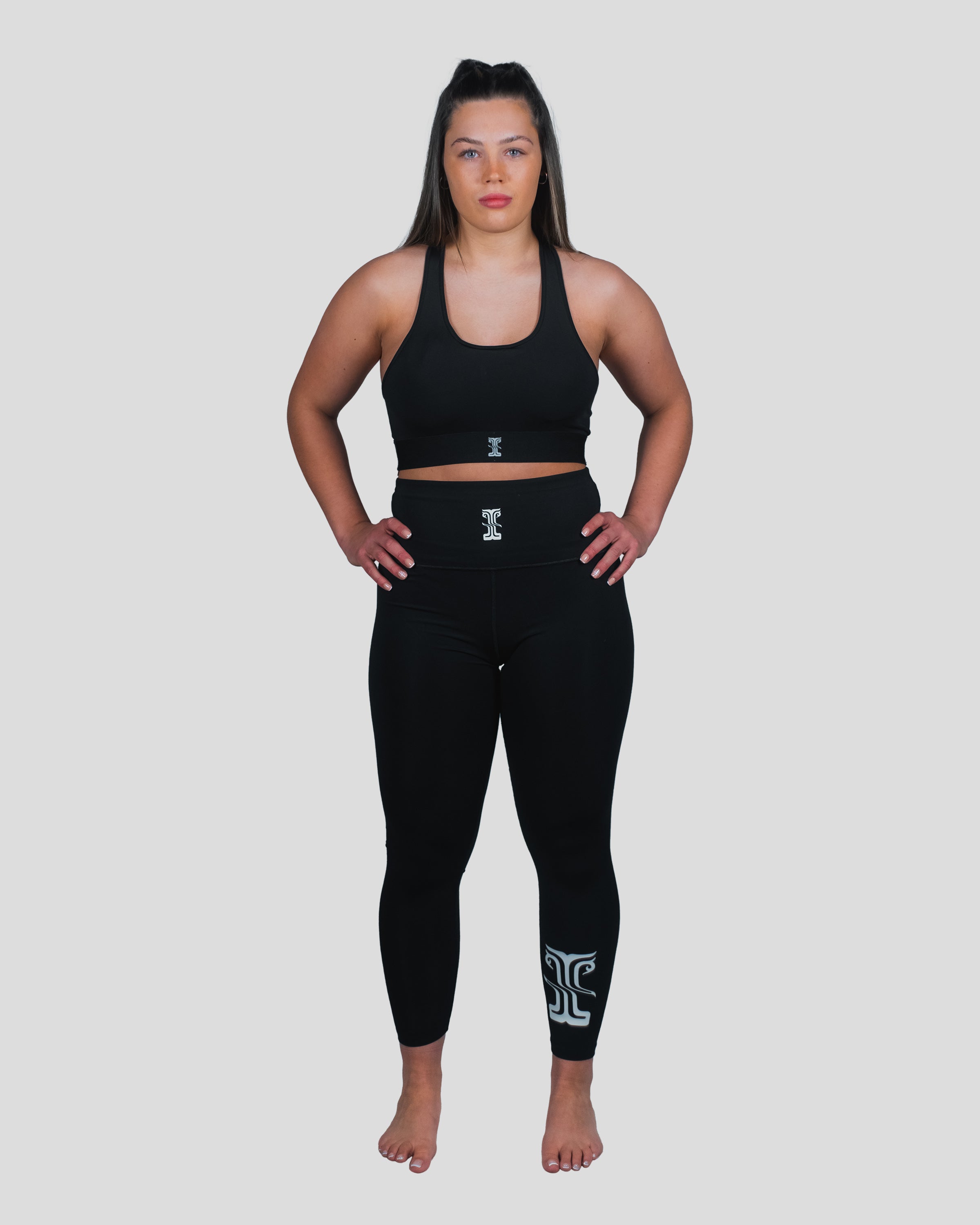 Woman wearing Gorgo Spats and a matching sports bra, standing in a strong stance, showcasing the sleek black design with high-waisted fit