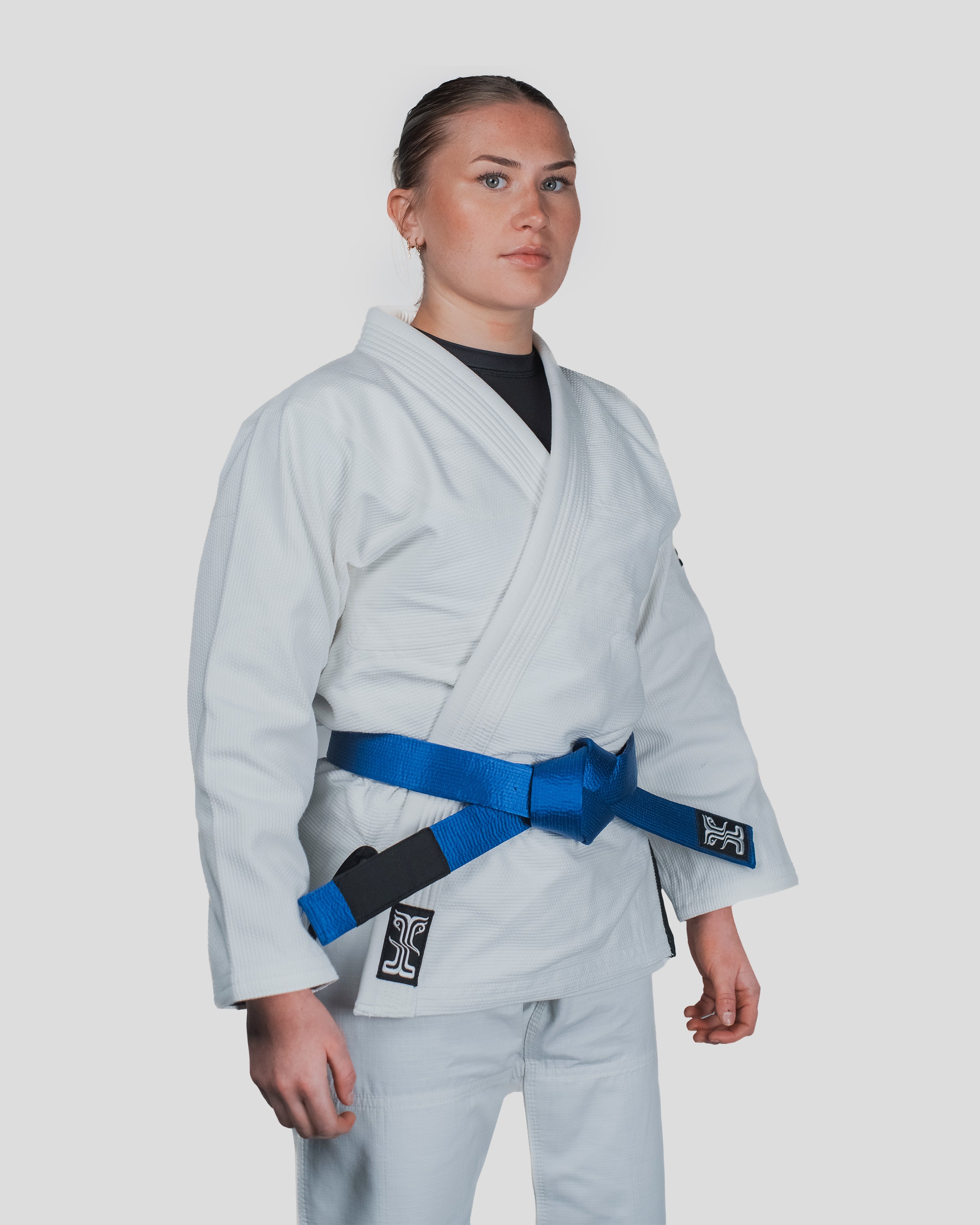 Front view of the Guile Women's Jiu Jitsu Gi in white, featuring a blue belt and premium cotton weave for maximum durability
