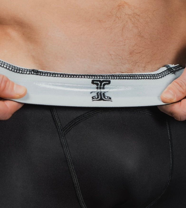 Close-up of the Persist Spats waistband being pulled, revealing the Kosmos logo on the inner lining for a premium finish